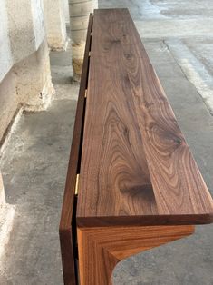 a wooden bench sitting on top of a cement floor next to a building with windows