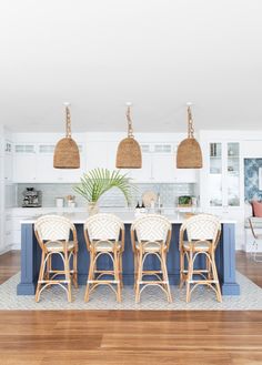 a kitchen with white cabinets and blue island in the center is surrounded by wicker pendant lights