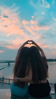 two women sitting on a bench with their hands in the shape of a heart over their eyes