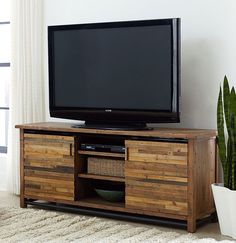 a flat screen tv sitting on top of a wooden entertainment center next to a potted plant