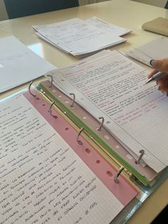 a person holding a pen and writing on top of a binder filled with papers