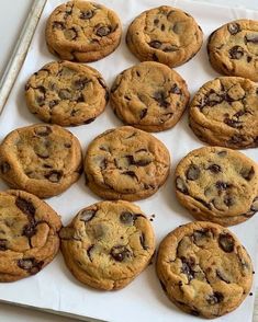 twelve chocolate chip cookies sitting on top of a white paper lined baking sheet, ready to be eaten