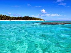 an island in the middle of clear blue water with palm trees on it's sides