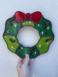 a hand holding up a stained glass christmas wreath ornament with red and green decorations