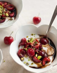 cherries and yogurt in a white bowl on a table with spoons