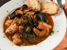 a white plate topped with shrimp and mussels next to bread on top of a table