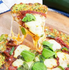 a slice of pizza being lifted from a wooden cutting board with basil and cheese on it