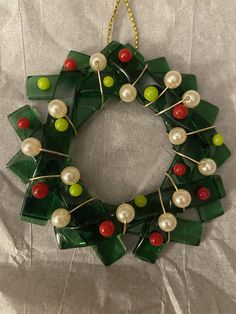 a christmas wreath made out of green and red glass with pearls on the front, hanging from a gold chain