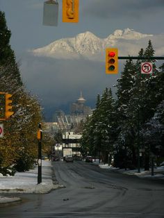 traffic lights and street signs on a city street with snow covered mountains in the background