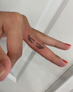 a woman's hand with an angel wing tattoo on her left thumb and red nail polish