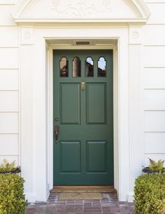 a green front door on a white house with brick walkway and potted planters