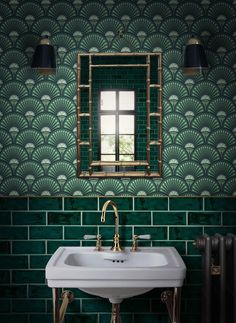 a white sink sitting under a mirror next to a green tiled wall with gold fixtures