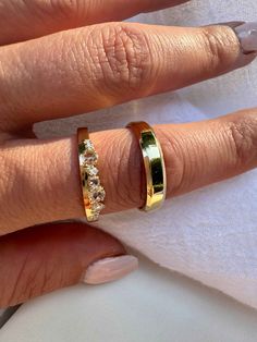 a woman's hand with two gold rings on her finger and one in the other