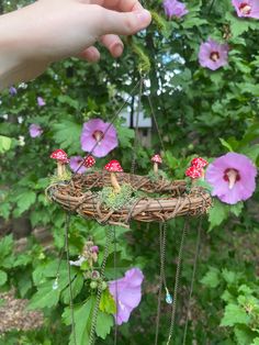 a person holding up a bird's nest with mushrooms and flowers in the background