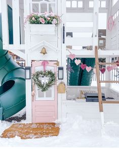 there is a pink door in the snow next to a green slide and flower pot