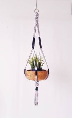 a potted plant hanging from a rope with a wooden bowl on the bottom and black handles