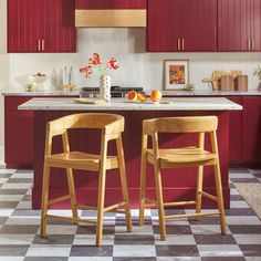 two wooden stools sit in front of a kitchen island with marble countertops and red cabinets