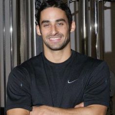 a man with his arms crossed standing in front of a metal door and smiling at the camera