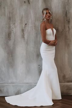 a woman in a white wedding dress standing against a wall with her hands on her hips