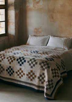 a bed with a quilt on top of it in a room next to a window