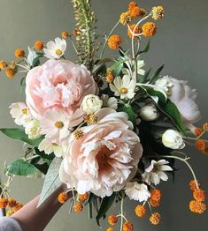 a bouquet of flowers is being held by a person's hand in front of a wall