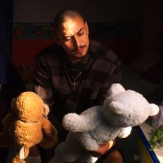 a man holding two teddy bears in his hands while sitting next to other stuffed animals