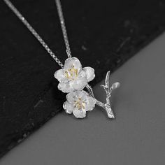 Introducing our exquisite pendant featuring a delicate design of cherry blossoms crafted in sterling silver. The intricate details of the flowers are beautifully highlighted with gold plating on the stamens, adding a touch of elegance and sophistication. The pendant captures the essence of spring, symbolizing renewal and beauty. It hangs gracefully from a matching sterling silver chain, making it a timeless accessory suitable for any occasion. Elegant Blossom Jewelry For Anniversary, Delicate Spring Jewelry For Anniversary, Delicate Jewelry For Spring Anniversary, Delicate Jewelry For Anniversary In Spring, Elegant Blossom-colored Spring Jewelry, Elegant Spring Blossom Colored Jewelry, Elegant Spring Anniversary Jewelry, Blossom Color Sterling Silver Flower Jewelry, Elegant Blossom Flower Pendant Jewelry