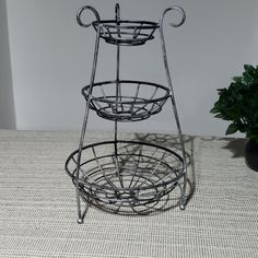 a three tiered metal basket on top of a table next to a potted plant