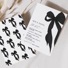 two black and white wedding cards with bows on them, next to some pampaste feathers