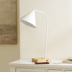 a white desk lamp sitting on top of a wooden table next to a dresser and drawers