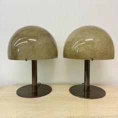 two lamps sitting on top of a wooden table next to each other, one is green and the other is brown