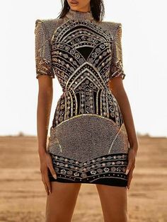 a woman standing in the desert wearing a short dress with an intricate design on it