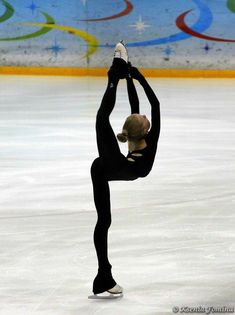 a female figure skating on an ice rink with her arms in the air and one leg up