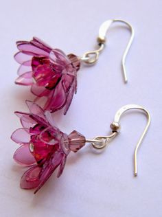 two pink flowers are hanging from silver earwires on a white surface, one is made out of glass and the other has metal hooks