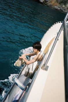 a boy sitting on the back of a boat holding a stuffed animal in his hands