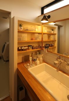 a bathroom sink sitting under a mirror next to a wooden shelf filled with bottles and containers