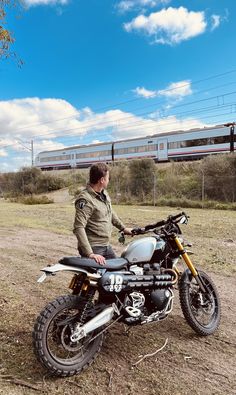 a man sitting on a motorcycle in the middle of a field with a train passing by