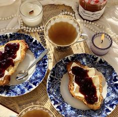 two blue and white plates with food on them next to a cup of coffee, candle and spoon