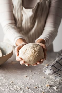 a person holding a ball of bread in their hands on a table with other ingredients