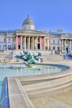 a fountain in front of a large building with columns and arches on the top floor