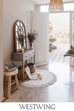 a room with a table, mirror and potted plants on the floor in front of an open door