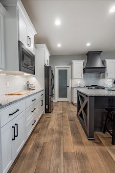 a large kitchen with white cabinets and wood flooring is seen in this image from the front view