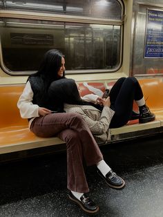 two people sitting on a subway bench looking at their phones