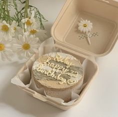 a birthday cake sitting in a box next to some daisies on a white table