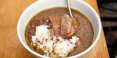 a white bowl filled with meat and rice on top of a wooden table next to an oven