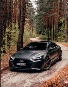 a black car driving down a dirt road in the woods