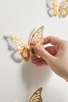 a hand holding a golden butterfly on a white wall with gold butterflies in the background