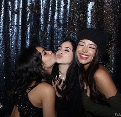 three young women are kissing each other in front of a sequin backdrop at a party