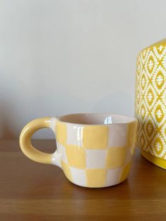 a yellow and white checkered coffee cup sitting on a table next to a vase