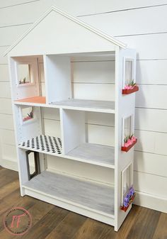 a white doll house with lots of shelves on the front and sides, sitting on top of a hard wood floor